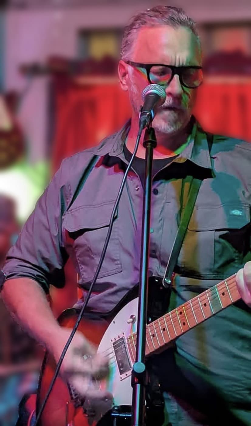 George singing and playing guitar on stage, under red and green lights
